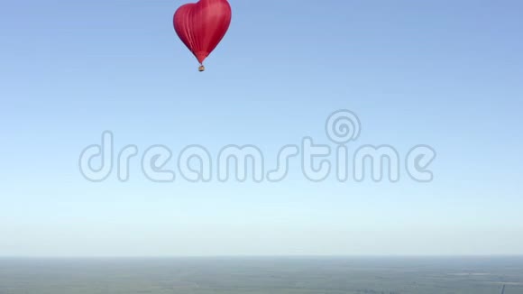 红色气球心形飞行在蓝天上绿色的视野中视频的预览图