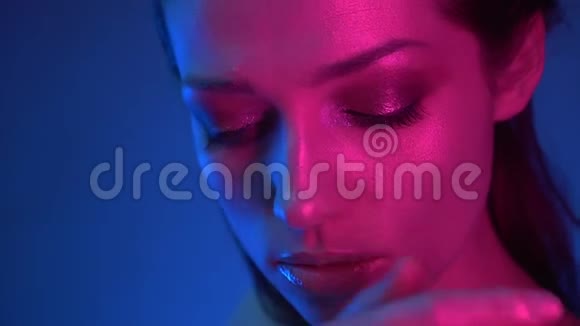 蓝粉色霓虹灯闪烁妆的模特特写镜头手指注视着她的脸视频的预览图