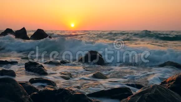 波浪在日落背景下拍打海滩上的岩石动作缓慢视频的预览图