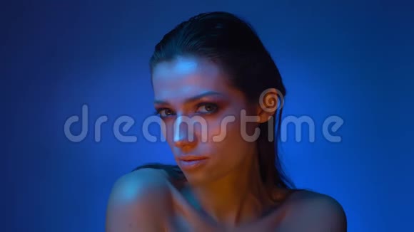 在蓝色霓虹灯中闪烁的时尚模特展示了她的脸的所有侧面进入相机视频的预览图