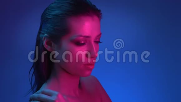 闪闪发光的模特在侧面闪闪发光的化妆在蓝色和粉红色的霓虹灯触摸她的肩膀和脸温柔视频的预览图
