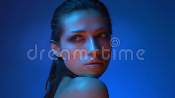 闪亮的模特站在蓝色霓虹灯中严肃地注视着肩膀进入相机视频的预览图