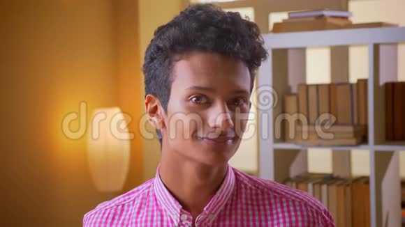 年轻迷人的印度男性在室内的大学图书馆里开心地看着镜头微笑的特写镜头视频的预览图