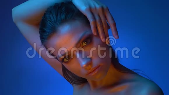发光模型与闪亮的化妆站在蓝色霓虹灯手放在头上注视相机固定视频的预览图
