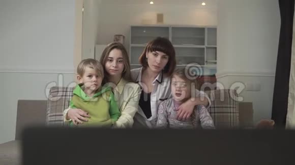 两个满脸愁容的姐姐和一个弟弟妹妹坐在客房的沙发上看电视视频的预览图