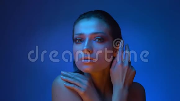 闪亮的未来时尚模特在冷蓝色霓虹灯触摸和覆盖她的脸与蓝色背景视频的预览图