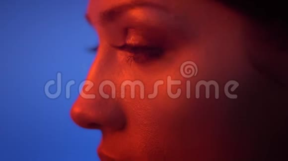 在蓝色背景的红色霓虹灯中时尚模特的眼睛和嘴唇轮廓的特写镜头是严肃的视频的预览图