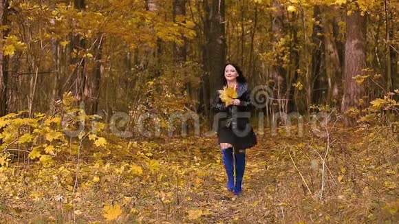 一位穿着蓝色靴子的年轻黑发女子正走在一个秋天的公园里手里拿着黄叶视频的预览图