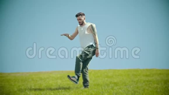 年轻时尚的男人穿着白衬衫在新鲜的草地上跳舞视频的预览图