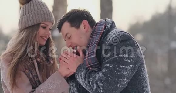 在一个白雪覆盖的公园里一个有爱心的男人在冬天温暖妻子的双手视频的预览图
