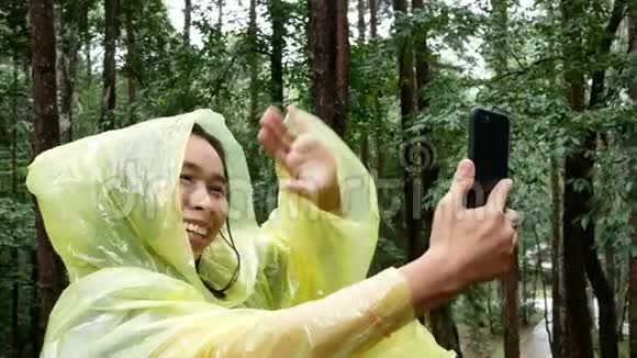 亚洲年轻女子自拍与智能手机在松林在下雨天视频的预览图