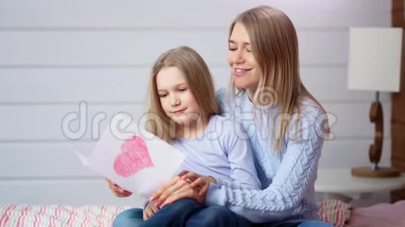快乐的妈妈和可爱的小女儿捧着红色的明信片庆祝快乐的妈妈一天视频的预览图
