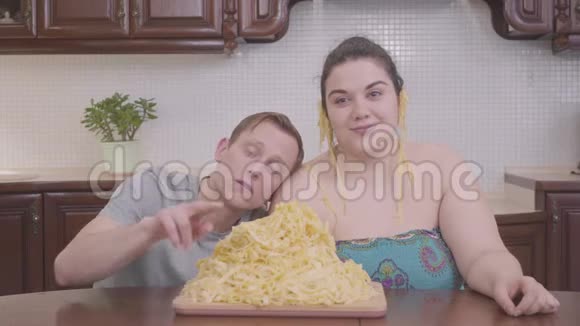 一位身材丰满的女人和一个金发的男人在厨房的餐桌前的一张大盘子里放着面条的画像视频的预览图