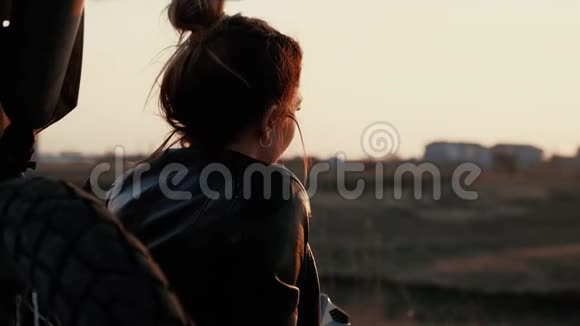 一个年轻的女孩坐在她的摩托车旁边欣赏日落视频的预览图