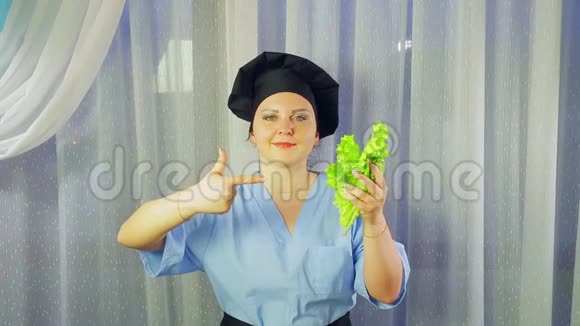 一个穿着围裙做饭的女人微笑着手里拿着一份绿色沙拉向它展示她的手视频的预览图