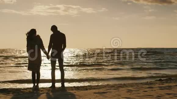 恋爱中的情侣看着海面上的夕阳牵着手凉爽的一天风在吹背面视频的预览图