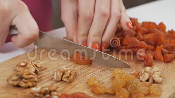 一位年轻的家庭主妇用一把刀在砧板上切果干杏子健康的饮食观念慢动作视频的预览图