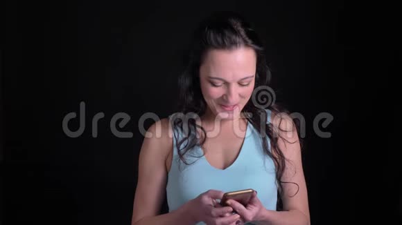 中年妇女在黑色背景下以愉快的兴趣观看智能手机的肖像视频的预览图