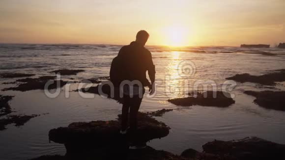 背包男的剪影站在海边看着美丽的金色日落慢动作视频的预览图