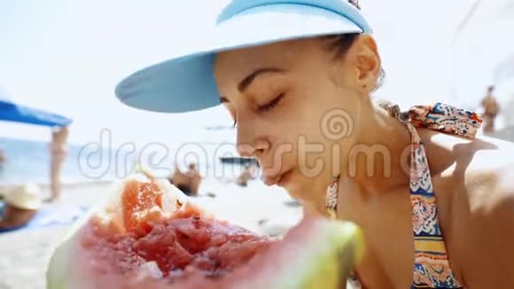 在海滩上吃一大块西瓜的滑稽少女的广角镜头视频的预览图