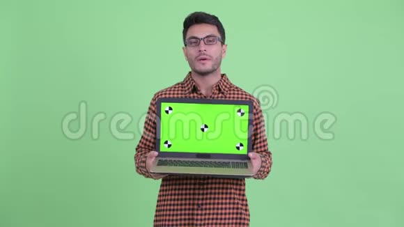 快乐的年轻西班牙裔时髦男人一边说一边展示笔记本电脑视频的预览图