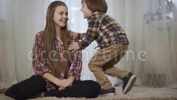 小女孩坐在客厅里毛茸茸的地毯上她哥哥来拥抱她家庭爱和幸福视频的预览图