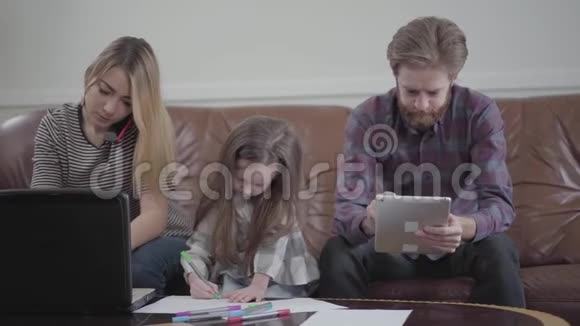 小女孩坐在母亲和父亲之间用彩色的标记画画年轻女子在她的笔记本电脑上打字视频的预览图