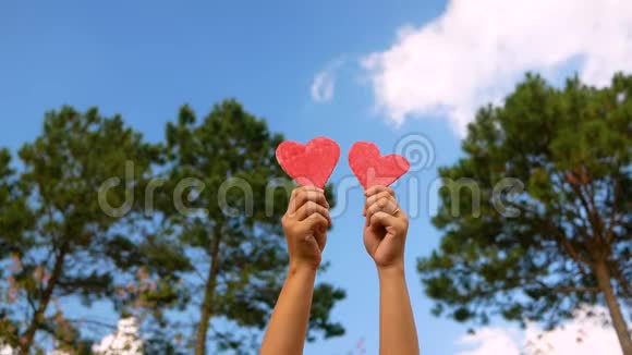 双手捧着红纸心形在蓝天绿树背景上随着音乐节奏翩翩起舞情人节的爱情象征视频的预览图