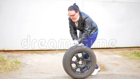 一个戴眼镜的女人在沥青上用圆盘卷着车胎视频的预览图