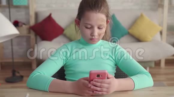 有面部缺陷的少女使用智能手机坐在家里的桌子旁视频的预览图