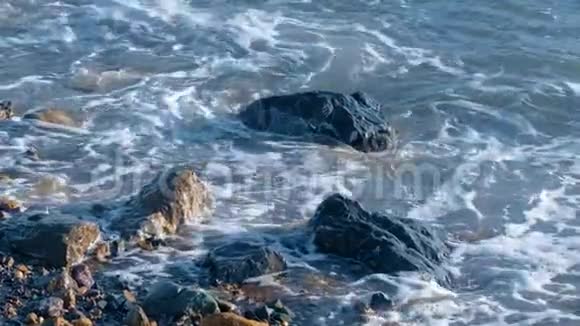 缓慢运动的海浪白色泡沫冲洗海滩上的鹅卵石和岩石视频的预览图