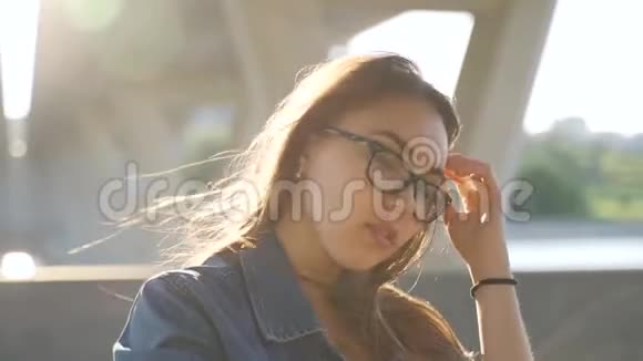 戴眼镜的女孩在桥的背景下为照相机摆姿势在风中飘扬的头发视频的预览图