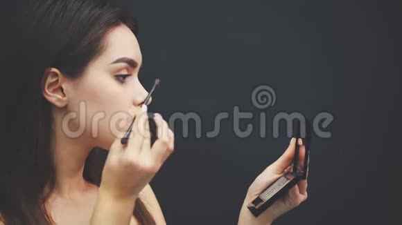 一个年轻女孩美丽的脸的特写得到一个化妆女人用刷子在眉毛上涂上眼影视频的预览图