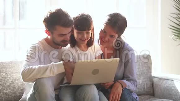 小女儿笑着看着笔记本电脑和父母一起看动画片视频的预览图