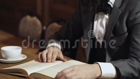 一个男人的特写手拿着一本打开的纸书用手指翻页喝茶男人手视频的预览图