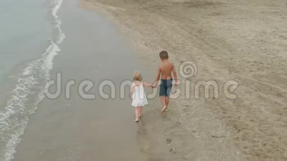 小男孩和小女孩牵着手沿着海滩奔跑视频的预览图