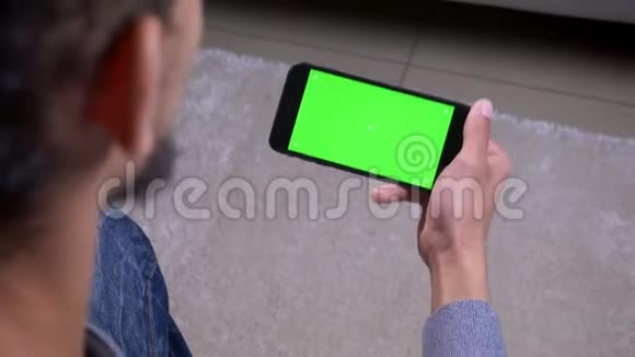 特写后景拍摄非裔美国男性博客作者流媒体直播手持绿色屏幕的手机在室内视频的预览图