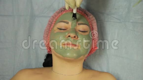 一位戴手套的男性美容师用特殊的刷子把一个泥面罩戴在客户的脸上视频的预览图