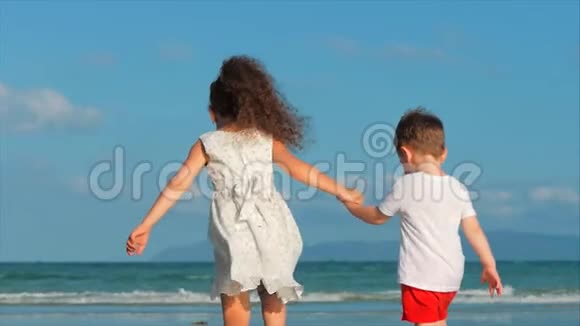 可爱的孩子女孩和男孩互相牵手沿着热带海岸奔向海洋概念视频的预览图