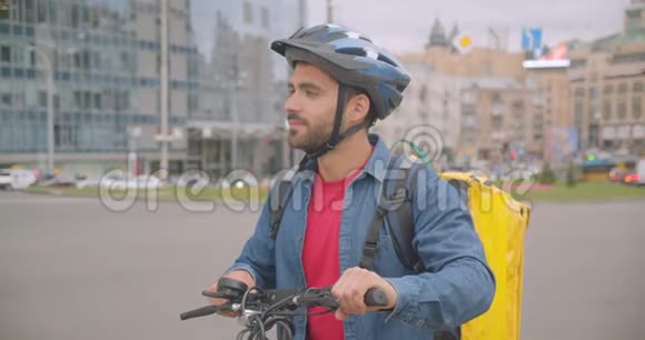 成人富吸引力的白种人送货员的特写肖像站着踢踏板车和背包看着摄像机视频的预览图