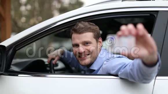 年轻的快乐男子坐在车里用大拇指显示他的新驾照视频的预览图