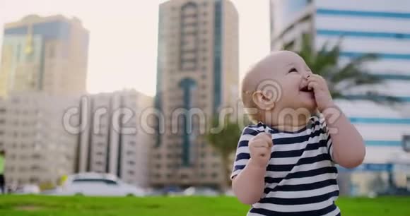 婴儿在夏天坐在背景建筑上的草地上笑视频的预览图