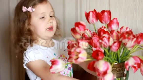 带着一束红色郁金香的快乐女婴孩子嗅着郁金香的气味生日和母亲节概念视频的预览图