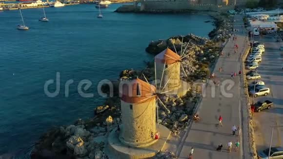 傍晚日落时分带着著名的风车著名的希腊罗德岛州曼德拉基港海滨的步行游客视频的预览图