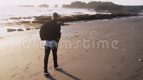 穿着时髦衣服的人背着背包沿着黑沙滩散步慢动作视频的预览图