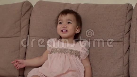 小女孩穿着漂亮的裙子坐在柔软的灰色沙发上笑着抬头看着视频的预览图