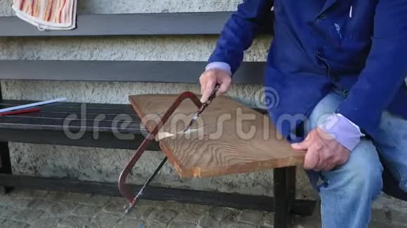 老人的手在野餐时用木头手锯在外面的地面上切割木板视频的预览图