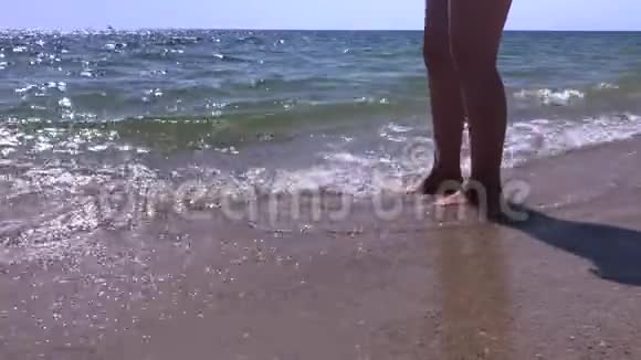 女人的脚站在沙滩上海浪拍打着她的脚在日出的海边慢动作美丽的海边镜头视频的预览图