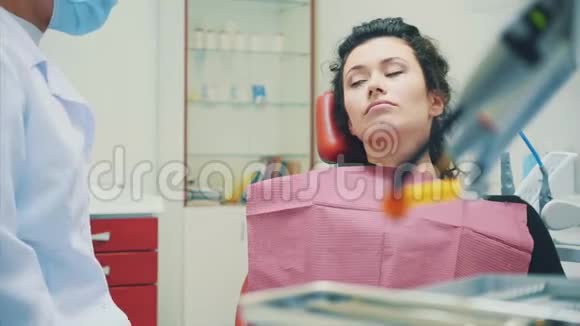 年轻女子坐在牙医的椅子上在医生的接待一个严肃的病人张开嘴视频的预览图
