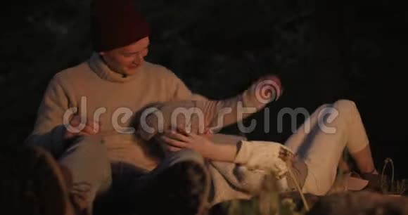 一个年轻的女孩晚上躺在她男朋友的膝盖上在篝火前的树林里他们做猴子视频的预览图